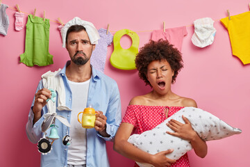 Tired exhausted young mother poses with baby on hand has sleepless nights while takes care of her...