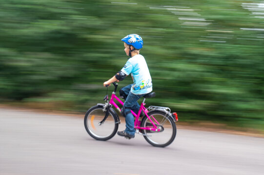 Junge auf rotem Fahrrad mit blauem Helm vor grünem Hintergrund