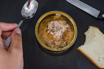 open can of salmon, a piece of bread and a spoon in hand on a black background.