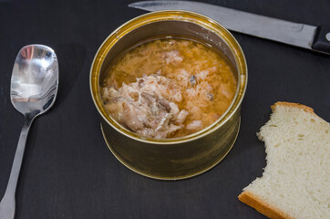 open jar of salmon, a piece of bread and a spoon on a black background. Snack on canned fish
