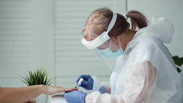 Manicurist in are wearing PPE paints nails in a beauty salon.  The existence of small businesses in isolation from COVID-19. A woman in a medical mask and rubber gloves makes a manicure