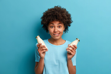 Horizontal shot of woman vegetarian holds two glass bottles of fresh lactose free milk dressed in...