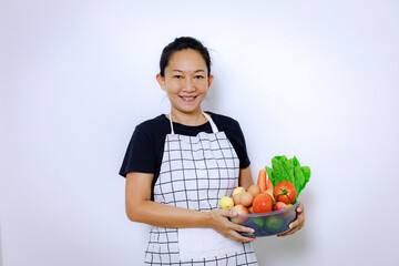 Naklejka na ściany i meble Asian Woman Standing Smile and Holding Mix Freshness Vegetables Box. Home Food Cooking and Housework Concept.