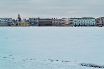Winter embankment of Saint Petersburg with colorful neat buildings stands on banks of frozen Neva river in snow. Crack in ice. European city