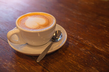 Soft focus of morning coffee, Heart-shaped milk coffee cup on the wooden table surface with advertising space, Hot coffee latte on a wooden floor with advertising space on the side.