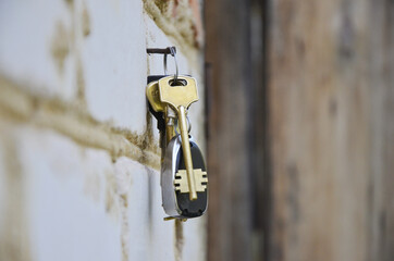 A bunch of keys hangs on a nail driven into the wall. Keys to real estate. Keys to the cottage. The lock is hanging in the open air. big yellow key. Pendant. Brick wall