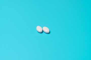 Two multivitamin pills or tablets for healthy diet nutrition on blue background. Copy space. Healthcare and medicine concept.