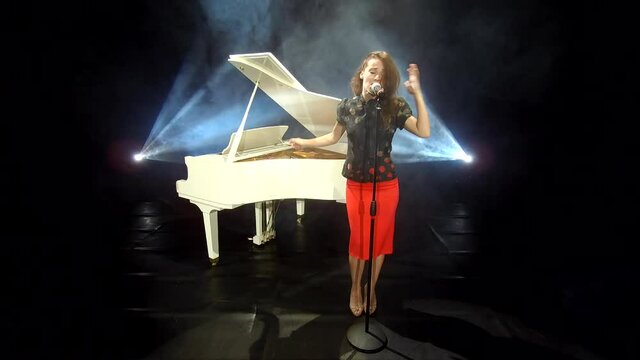 sexy girl in classical vintage wear on stage. stage live performance. vocal show. singer with piano forte and microphone. smoke and stage lights. retro woman singing blues. jazz music.