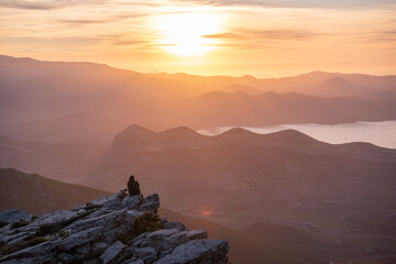 Young woman enjoying beautiful sunset scenery from the peak of a mountain