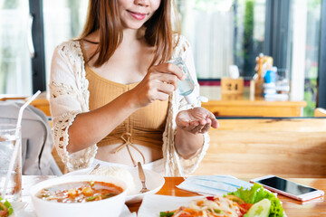 Beautiful young Asian woman applying hand sanitizer onto her hand before eating in restaurant for disinfection virus, bacteria and germs. Coronavirus Covid-19, health care and new normal concept.