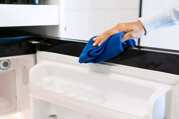 Woman hand with micro fiber cloth wiping refrigerator surface. Home, housekeeping concept.