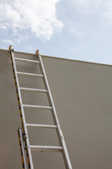 Ladder aluminium on grey wall. Below to upper front view, vertical, blue sky background.