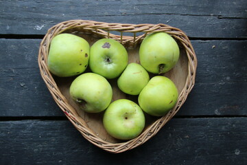 Ripe green apples on the table in a heart-shaped basket
