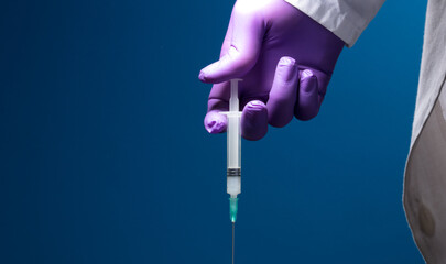 Syringe, medical injection in the hand, palm or fingers. Plastic vaccination kit with needle. Nurse or doctor. Liquid or narcotic drugs. Health care in hospital.Blue background
