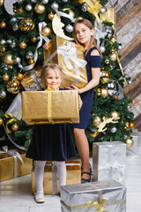 Sisters holding wrapped presents standing beside decorated Christmas Tree at home on Boxing Day