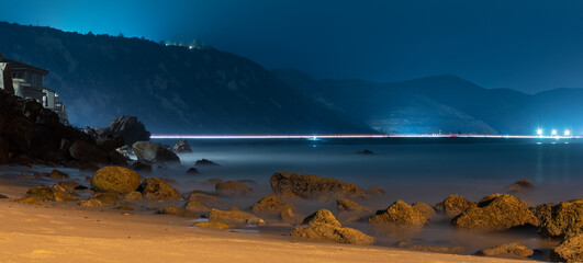Barnacle covered rocks withstand the ocean tide as streaking headlights show on the distant 101...