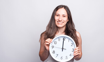 Portrait of beautiful young woman smiling and holding big white clock at twelve a clock