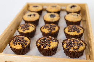 Close-up image of batch of homemade, chocolate cupcakes in paper cake cases on circular, black, metal wire cooling rack, chocolate butter chocolate pieces and blueberry