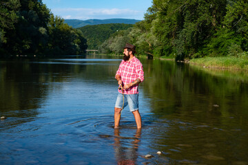 Brutal man stand in river water. Happy fly fishing. Handsome man relaxing. Men bearded fisherman. Relax in natural environment. Fly fish hobby of man in checkered shirt. Fishing.