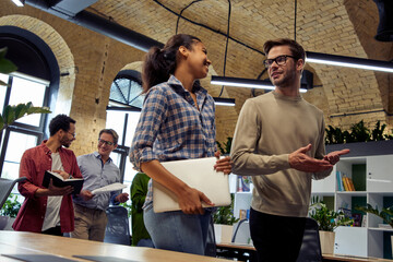 Two young diverse business people, male and female coworkers talking about something while walking in the modern office