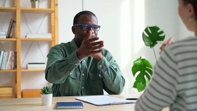 Male hr manager interviewing female job seeker during working day at modern office spbas. African American businessman is talking to woman and shaking hands while sitting at table in bright room