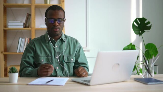 African American businessman talking during online meeting at table with laptop in company spbas. Young man having conversation and looking at computer screen while sitting at comfortable workplace in