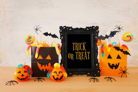 holidays image of Halloween. Pumpkins, bats, treats, paper gift bag over wooden table