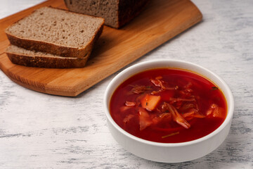 Vegetarian borscht in a white tureen on a light wooden table next to slices of wholemeal bread.