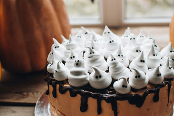 Sweets for halloween party on a wooden table. Halloween style party, candy bar and decorations with pumpkins. Halloween cake, mousse cake for the holiday and ghost shaped meringue.