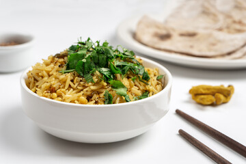 Khichdi in a white plate next to the bread sticks and condiments