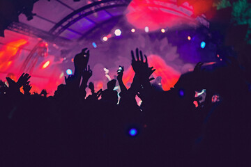 Abstract blur atmosphere: happy people enjoying outdoor music festival concert, raised up hands and clapping of pleasure, active night life concept, play of light and shadow on the stage