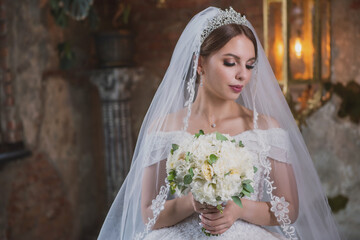 Fototapeta na wymiar bride in a wedding dress and a bouquet in a beautiful old hall with chandeliers