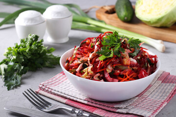 Salad from fresh vegetables: cabbage, beet, carrot, cucumber, onion and parsley in white bowl on gray background, Closeup. Horizontal format