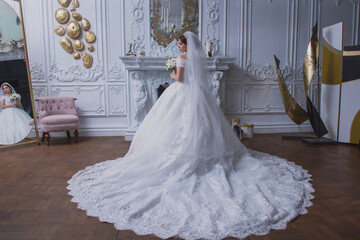 bride in a wedding dress with a long train and a bouquet in an old hall with chandeliers
