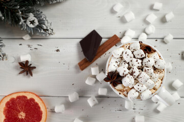 Mug of hot coffee with marshmallows sprinkled with chocolate, anise, cinnamon and a slice of dried grapefruit on white wooden table. Winter hot drink.