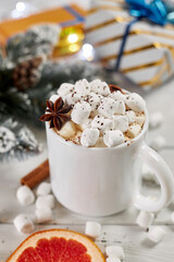 Mug of hot coffee with marshmallows sprinkled with chocolate, anise, cinnamon and a slice of dried grapefruit on white wooden table. Christmas concept. Winter hot drink and gift boxes.