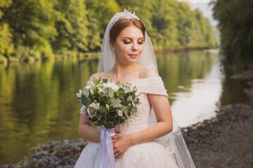 bride in a wedding dress with a long train and a bouquet against the backdrop of a mountain river, forest and rocks