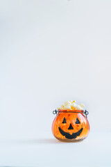 Bowl in the shape of a jack-o-lantern orange pumpkin container with popped popcorn on the white background. Halloween movie night concept. Vertical card. Selective focus. Copy space.