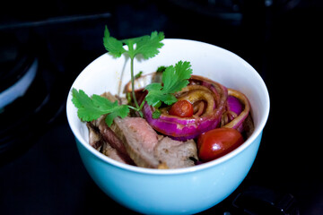 Preparing a roast beef lunch in a Brazilian cuisine, with red onions, cherry tomatoes and more spices and also using a red tongs to facilitate the cooking of the meat. Cooking concept. Food concept
