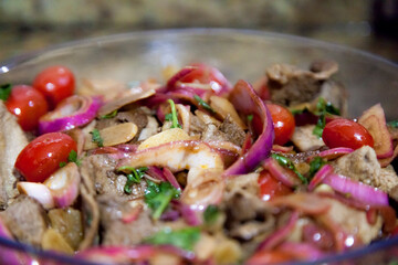 Preparing a roast beef lunch in a Brazilian cuisine, with red onions, cherry tomatoes and more spices and also using a red tongs to facilitate the cooking of the meat. Cooking concept. Food concept
