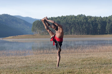 Indian Kalaripayattu warrior doing yoga exercise on green grass in Kerala, South India