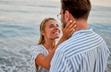 A loving young couple hug on the seashore, enjoying each other and their vacation. A woman in a dress and a man in a shirt are romantically spending time on the beach.