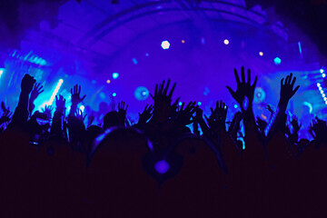 Abstract blur atmosphere: happy people enjoying outdoor music festival concert, raised up hands and clapping of pleasure, active night life concept, play of light and shadow on the stage