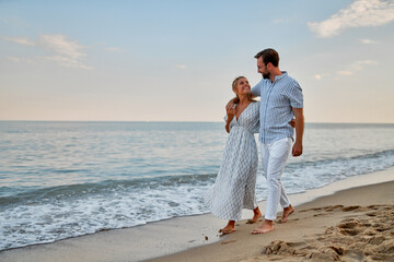 A young couple in love are walking along the seashore, enjoying each other and their vacation,...