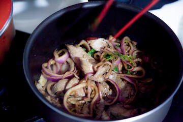 Preparing a roast beef lunch in a Brazilian cuisine, with red onions, cherry tomatoes and more spices and also using a red tongs to facilitate the cooking of the meat. Cooking concept. Food concept
