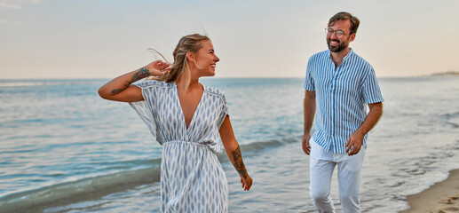A loving young couple run along the seashore, enjoying each other and vacation, having fun on the beach.