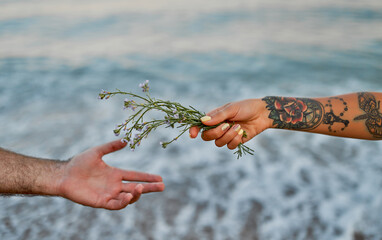 Close-up image of male and female hands with flowers on the background of the sea.