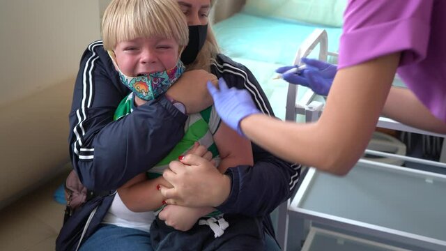 The doctor vaccinates the child. The boy is crying during vaccination. Shot in the shoulder. Vaccination against the flu and Covid-19
