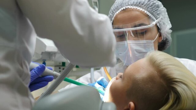Female doctor while dental treatment wearing plastic protective shield, Doctor in facial protection: mask and screen. Young boy getting toothcare procedure. Close-up. 4 k video