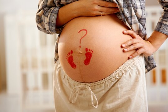 Close-up of pregnant belly with little drawn footprints and question mark.
